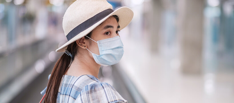 Young adult female wearing face mask in airport terminal, protection Coronavirus disease infection, Asian woman traveler walking on escalator in aerodrome. New Normal and travel under COVID-19 concept