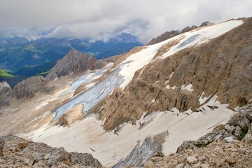 View from Marmolada summit. Sharp rocks with glacier, green meadows in the background. Clouds. Dolomites Mountains. 