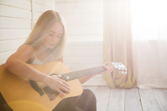 Attractive woman with guitar sitting in light room with wooden floor. Musician, concert, hobby, leisure, rehearsal concept