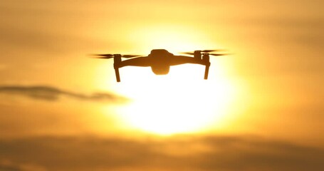 A silhouette Quadrocopter flies at sunset.sunset, drone in the sunset sky,A drone taking pictures of aerial views - Powered by Adobe