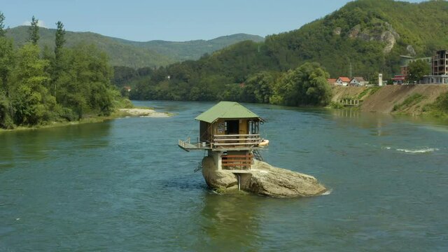 Aerial shot Serbia. Drone video in which a small house stands on a rock in the middle of the river where you can see the rocks, water, forest and trees, and the landscape. On a background of beautiful