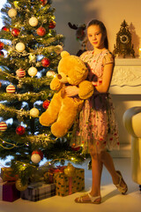 Teenage Girl Standing near Christmas Tree Holding Big Teddy Bear