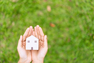 Close-up of hand holding wooden house model with green natural and sunlight background