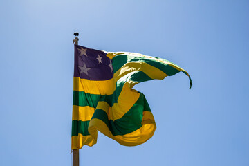 Bandeira de Goiás, tremulando ao vento com céu azul ao fundo.