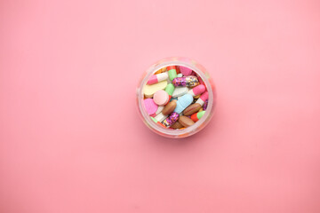 Fototapeta na wymiar top view of colorful pills in a container on pink background 