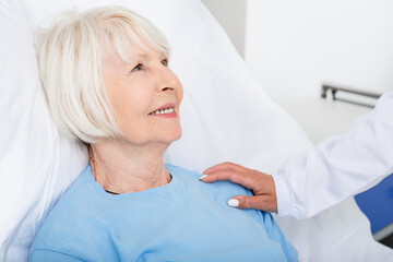 Medical care for the senior patient in the hospital. Elderly woman smiles and feels the support of a doctor, while in a hospital bed