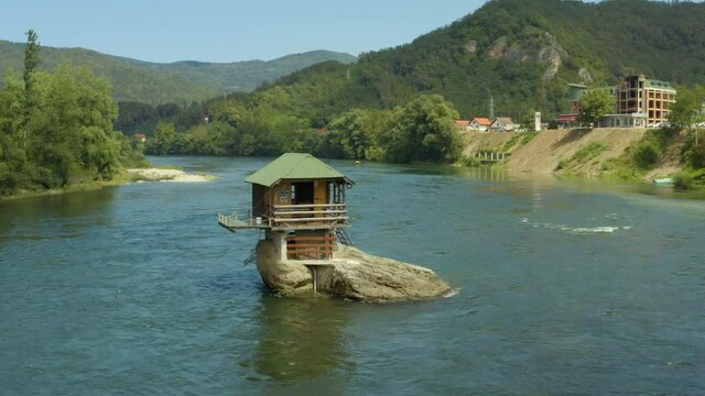 Aerial shot Serbia. Drone video in which a small house stands on a rock in the middle of the river where you can see the rocks, water, forest and trees, and the landscape. On a background of beautiful