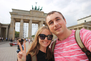 Happy smiling couple of tourists taking selfie photo on background of Brandenburg Gate in Berlin. © Serhii