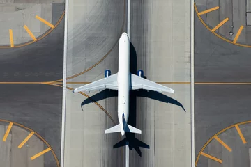 Foto op Plexiglas Luchtfoto van vliegtuigen met een smal lichaam die de landingsbaan van de luchthaven verlaten. Bovenaanzicht van wit niet-geïdentificeerd vliegtuig in het midden van taxibaanlijnen. Luchtvaartindustrie. © Thiago Trevisan