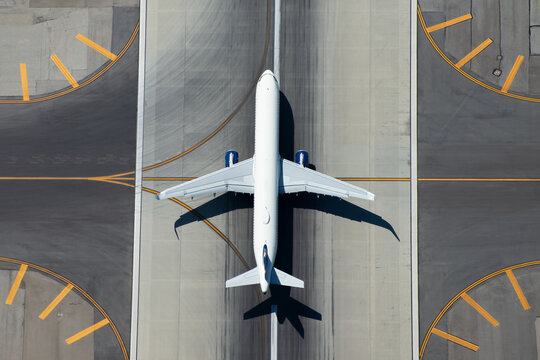 Aerial view of narrow body aircraft departing airport runway. Top down view of white unidentified airplane in the center of taxiway lines. Aviation industry.