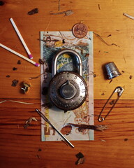 Flay lay consisting of an old combination lock set atop a New Zealand bill surrounded by odds and...