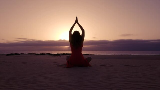 Woman greeting the sun with a yoga pose on the beach in the morning