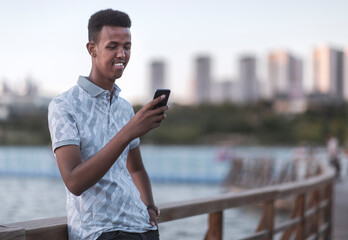 Young black man in casual clothes typing a sms with his mobile phone, copy space includes