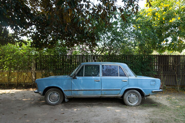 Fototapeta premium The old, abandoned blue car in a garden