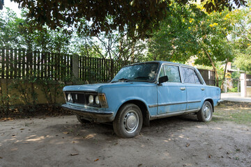 The old, abandoned blue car in a garden