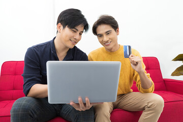 asian two men homosexual or gay couples holding credit card and shopping online with computer laptop on sofa