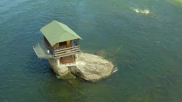 Aerial shot Serbia. Drone video in which a small house stands on a rock in the middle of the river where you can see the rocks, water, forest and trees, and the landscape. On a background of beautiful