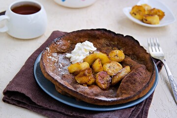 Chocolate Dutch Baby pancake with caramelized bananas on a gray plate on a light concrete background. Selective focus. American cuisine.