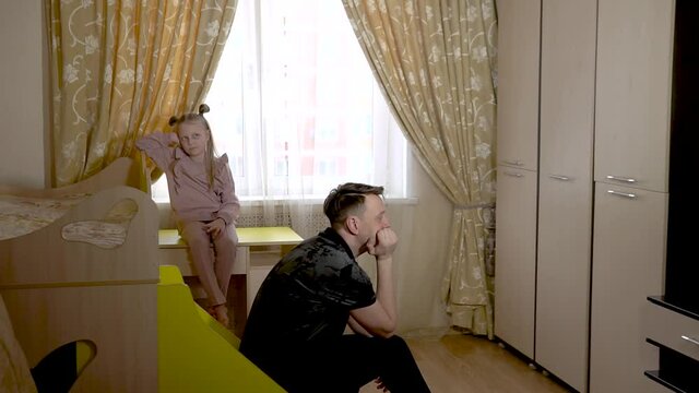 Think the old dad sits on the stairs on wheels with a joyful little girl in a large living room in home clothes. On against the crib and the sofa.