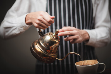 barista pouring hot water from the kettle over the coffee powder to extract making the freshly brewed coffee in the coffee cafe.