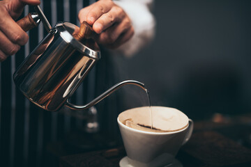 barista pouring hot water from the kettle over the coffee powder to extract making the freshly...