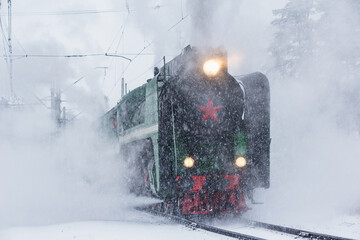 Retro steam train departs from the railway station at winter snowy time.