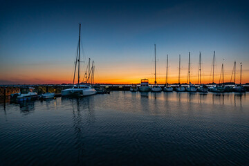 Fototapeta na wymiar Beautiful sunset of a harbour with reflections in calm water with sailing boats and motor yachts