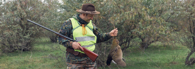 Hunter man in rural field with shotgun and backpack during hunting season