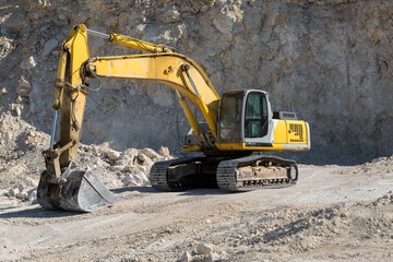 A large yellow tracked excavator is mining rock in a quarry.