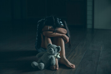 Sad little child girl sitting alone with teddy bear on floor