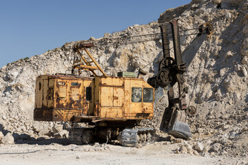 A large yellow tracked excavator is mining rock in a quarry.