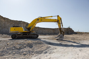 A large yellow tracked excavator is mining rock in a quarry.