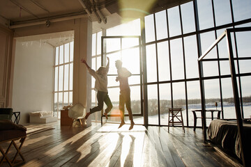 Two happy people are jumping and rejoicing in their new loft apartment. A young family bought a house with a mortgage loan - obrazy, fototapety, plakaty