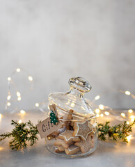 Christmas homemade cookies in a glass jar with the letters Gift. New Year and Christmas card. blurred background with Christmas lights. copy space. vertical image.