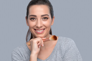 Portrait of a beautiful brunette woman with beautiful fresh makeup and healthy clean skin holding a powder brush in her hand. Professional makeup and skin care cosmetology.