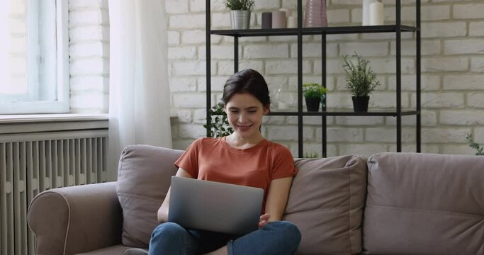 Girl spend free time use internet fun rest sit on sofa in living room put laptop on laps smiles enjoy lazy weekend chatting in social media network, watch movie, funny videos modern tech usage concept