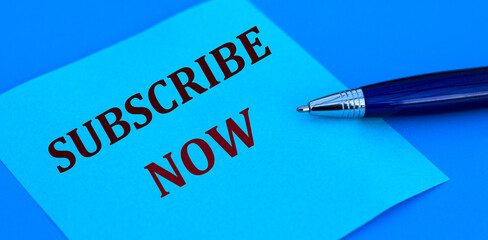 SUBSCRIBE NOW words written with a pen on blue paper on a blue background