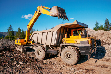 Mining dump truck in the highlands. The excavator loads the mountain soil with a bucket into the body of a dump truck © Letopisec