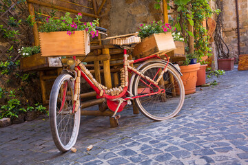 A classic red bike is decorated with wine corks and crates on a cobblestone street in Orvieto, Italy
