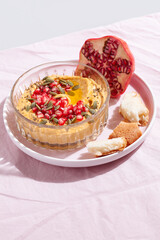 Pumpkin hummus dip with pomegranate and seed topping on pink textile background. Healthy Thanksgiving vegetarian appetizer