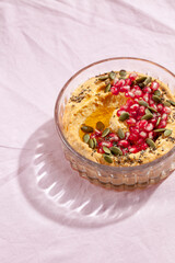 Pumpkin hummus dip with pomegranate and seed topping on pink textile background. Healthy Thanksgiving vegetarian appetizer. Top view