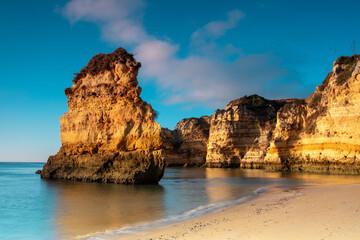 Landscape photo. Scenic rocks on the beach. Blue sky and still water. Lagos, Algarve Coast, Portugal