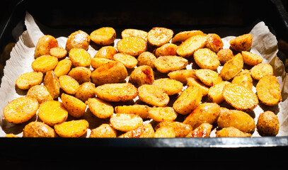 Baked appetizing crispy potato on baking tray. Side view. Close-up.