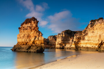 Landscape photo. Scenic rocks on the beach. Blue sky and still water. Lagos, Algarve Coast, Portugal