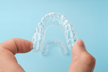 Close up mans hand holding invisible aligners for whitening and straightening of teeth on the blue...