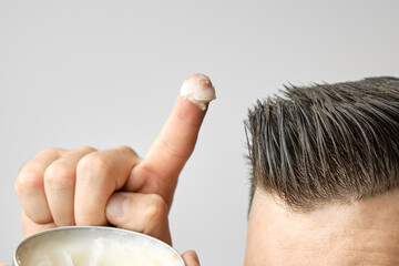 Man applying a clay, pomade, wax, gel or mousse from round metal box for styling his hair after...