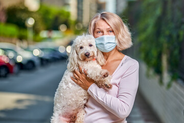 Woman an antivirus mask with a dog on a city street