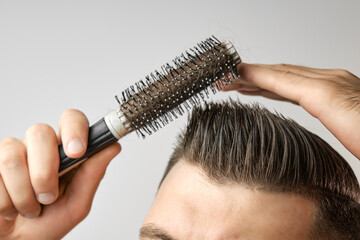 Man using a round brush for styling his hair. Hair care at home after barbershop. Combing of short brown hair on the white background