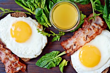 Breakfast fried eggs with bacon, fresh spinach, arugula and orange juice.