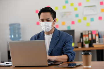 Asian senior business man in casual wearing mask working with laptop in modern office or co-working space Due Covid-19 Flu Pandemic,Health care and Business Startup Concept